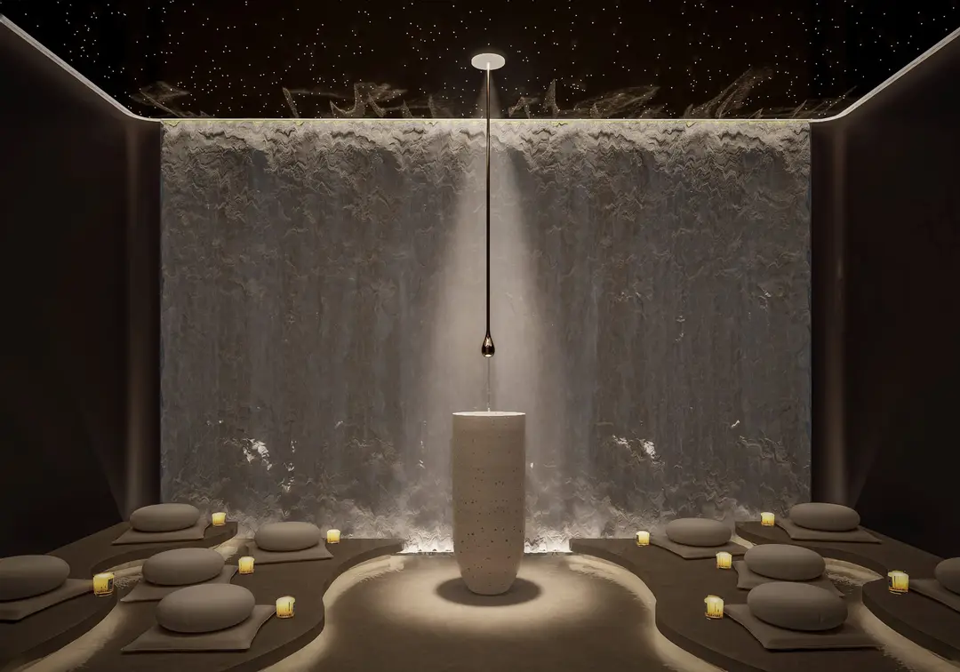 Sala de meditación con muro de agua, cojines y una fuente de piedra al centro